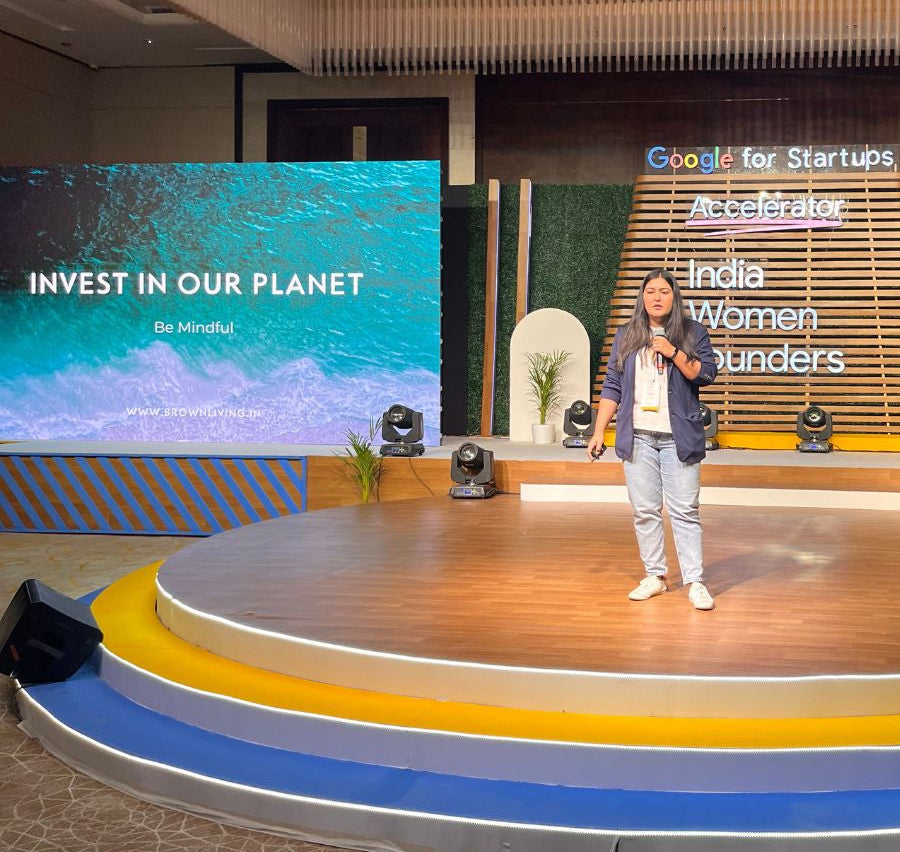 Chaitsi Ahuja on a stage with a large screen displaying 'Invest in Our Planet' at an event.